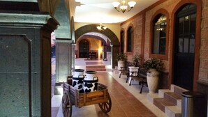 A lobby with a wooden cart, stone arches, and potted plants. - Hotel Villa Bernal (Ezequiel Montes)
