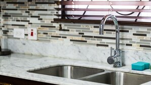 A kitchen with a stainless steel sink, a faucet, and a tiled backsplash. - New Kingston Apartment at The Palms (Kingston)