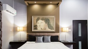 A hotel room with a large bed, two bedside tables, a wall-mounted air conditioner, and a framed artwork above the bed. - New Kingston Apartment at The Palms (Kingston)