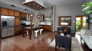 A modern kitchen with stainless steel appliances, wooden cabinets, and a dining area with a table and chairs. - New Kingston Apartment at The Palms (Kingston)
