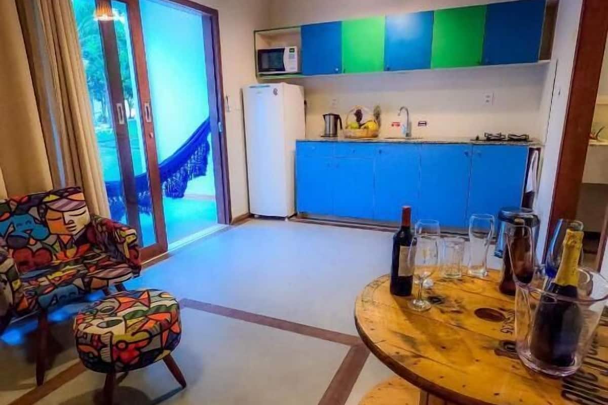 A modern living room with a colorful sofa and a wooden coffee table, a kitchen with blue cabinets, and a sliding glass door leading to a balcony.