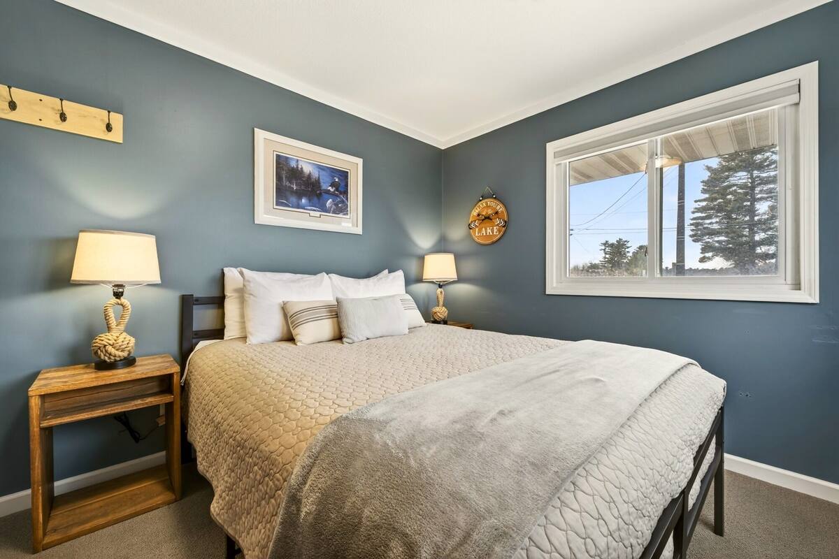 A bedroom with a bed, two bedside tables, a window, and a wall-mounted picture.