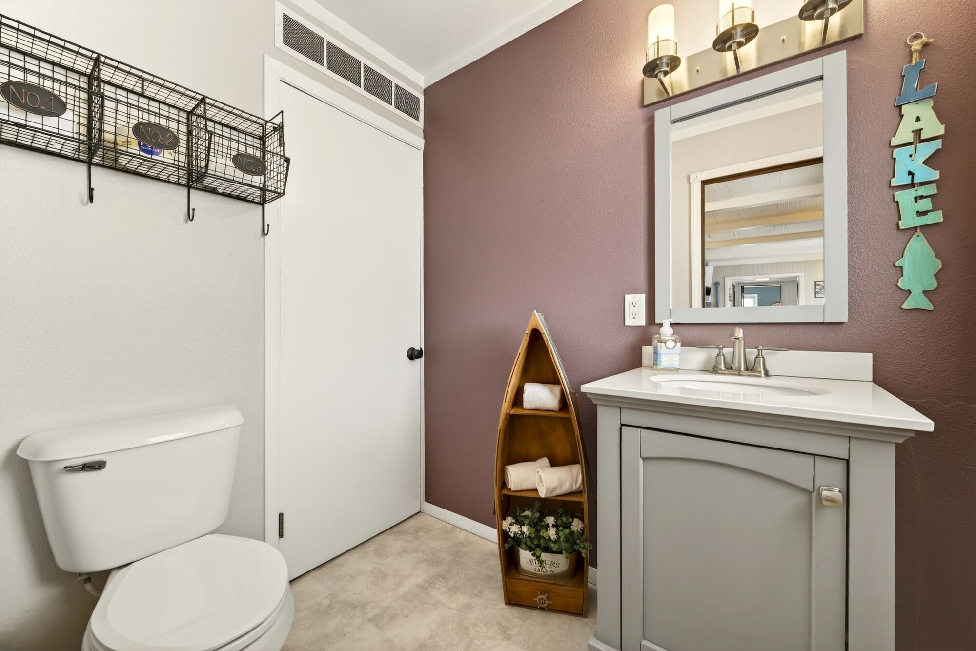 Une salle de bain comprenant des toilettes, un meuble-lavabo avec un miroir, une étagère avec des serviettes et un luminaire fixé au mur.