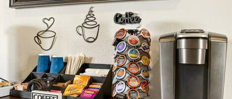 Una estación de café con una cafetera, un cuadro decorativo con motivos de café y un portalapilas para tazas de café.