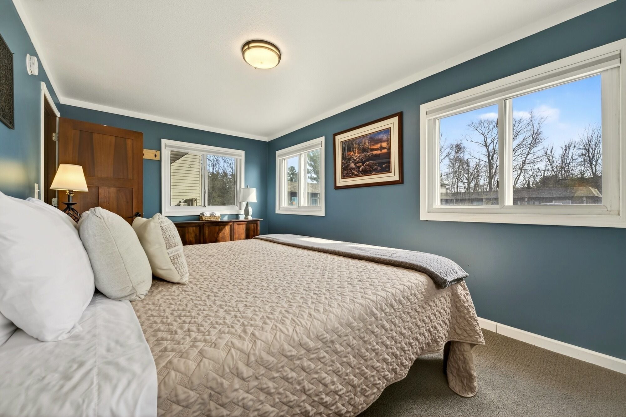 A bedroom with a bed, two windows, a dresser, and a lamp.