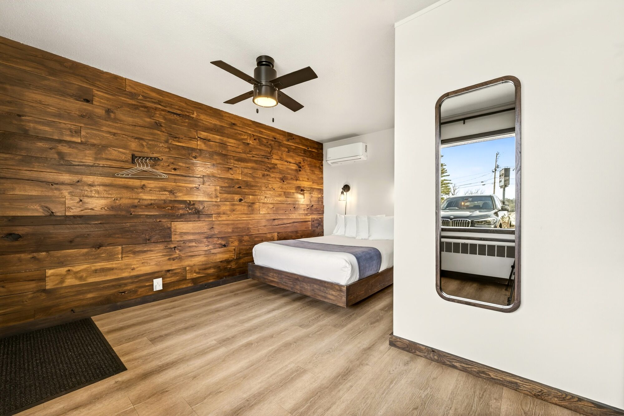 Ein Schlafzimmer mit Holzwand, Deckenventilator, Bett, Spiegel und Klimaanlage.