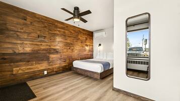 Ein Schlafzimmer mit Holzwand, Deckenventilator, Bett, Spiegel und Klimaanlage.