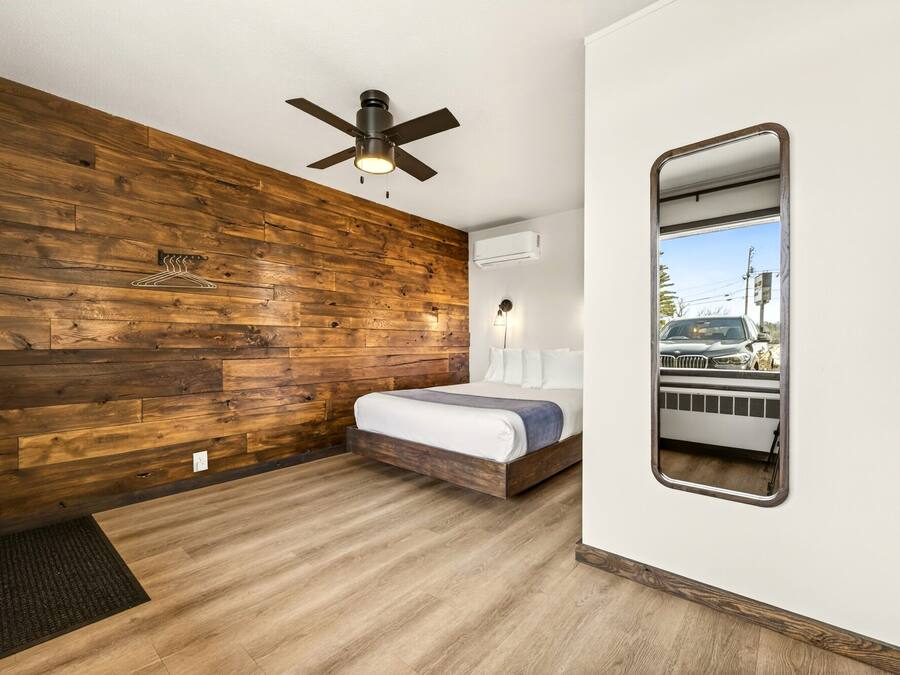 Ein Schlafzimmer mit Holzwand, Deckenventilator, Bett, Spiegel und Klimaanlage.