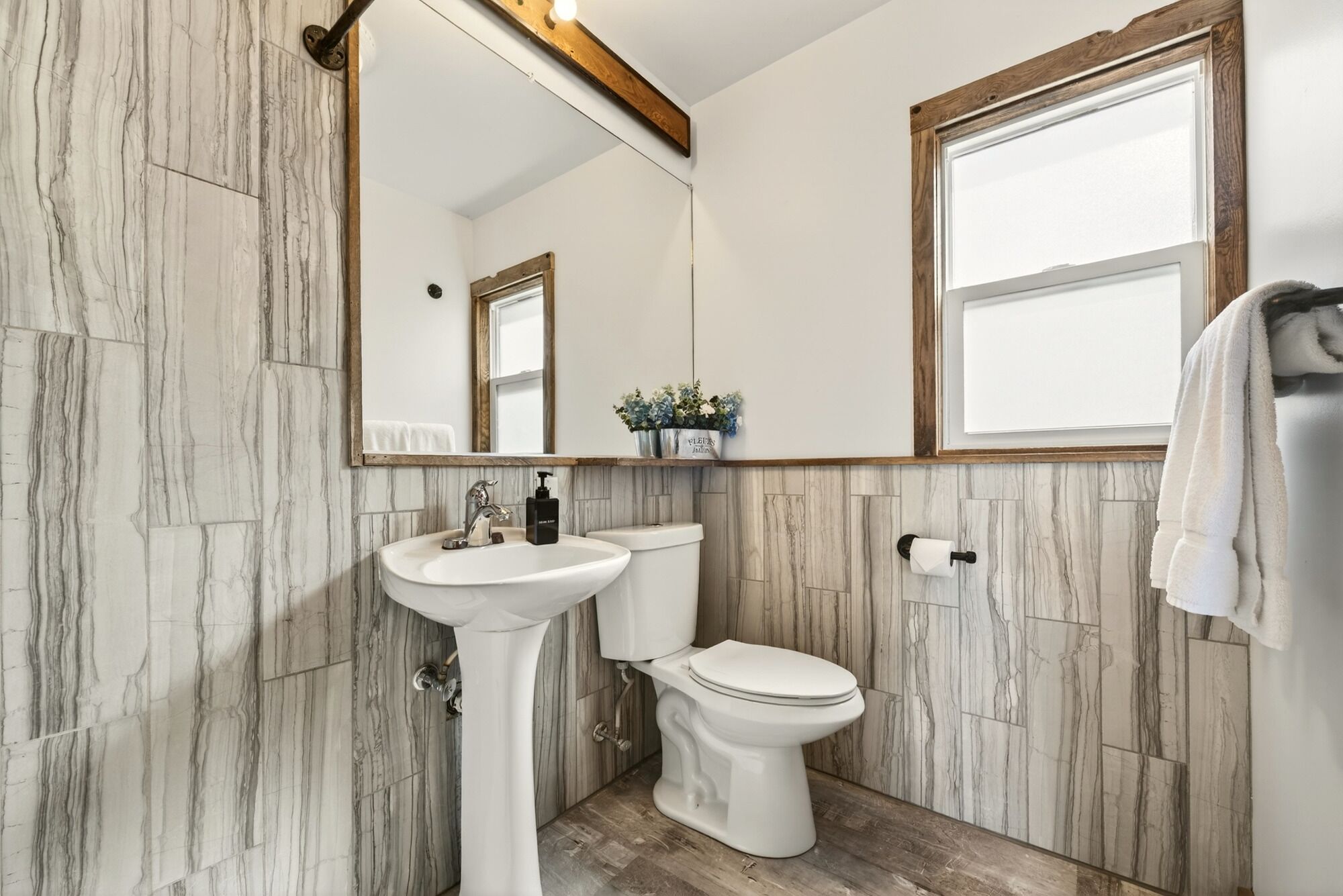 Een badkamer met een marmeren wand, een wastafel op een voetstuk, een toilet en een spiegel met houten lijst.