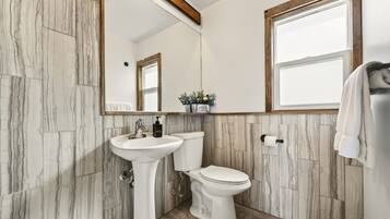 Een badkamer met een marmeren wand, een wastafel op een voetstuk, een toilet en een spiegel met houten lijst.