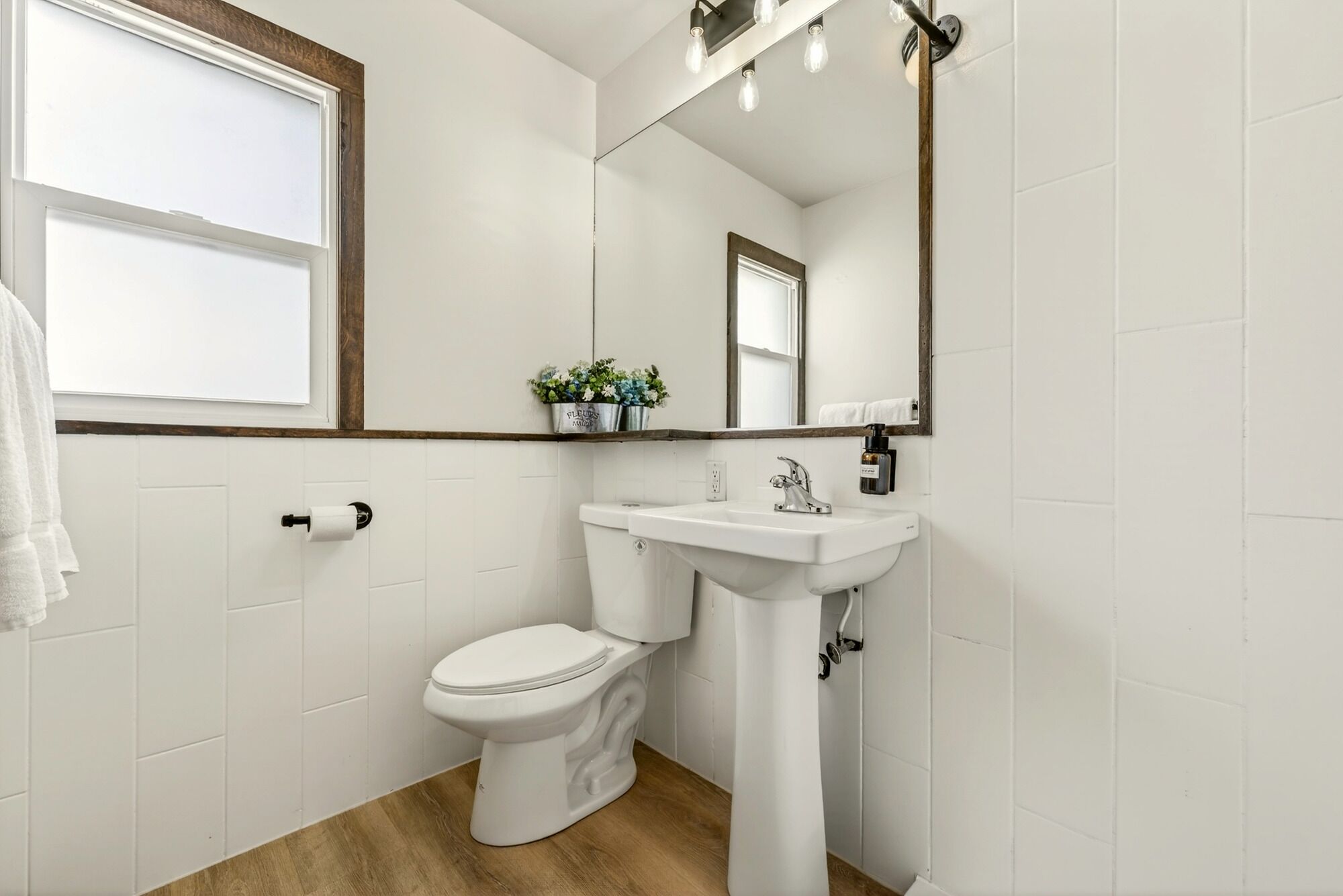 A bathroom with a toilet, sink, mirror, and a window.