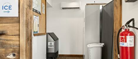 A narrow hallway with a sign for ice cubes, a white trash bin, a fire extinguisher, and a wall-mounted air conditioning unit.