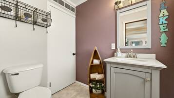 A bathroom with a toilet, a vanity with a mirror, a shelf with towels, and a small plant.