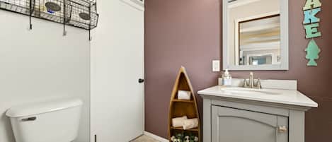 Un baño con inodoro, tocador con espejo, repisa con toallas y una planta pequeña.