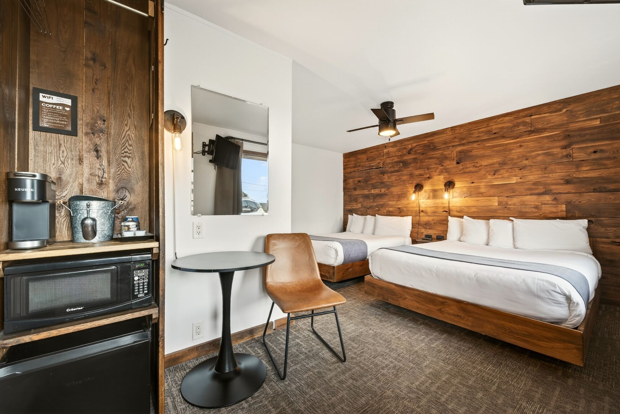 Habitación de hotel con cama, una silla, una mesa, microondas, cafetera y pared de madera.