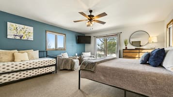 A bedroom with a bed, a sofa, a chair, a ceiling fan, a TV, a window, and a mirror.