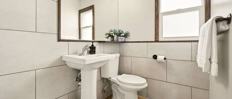 Un baño con lavamanos, inodoro y espejo blancos.