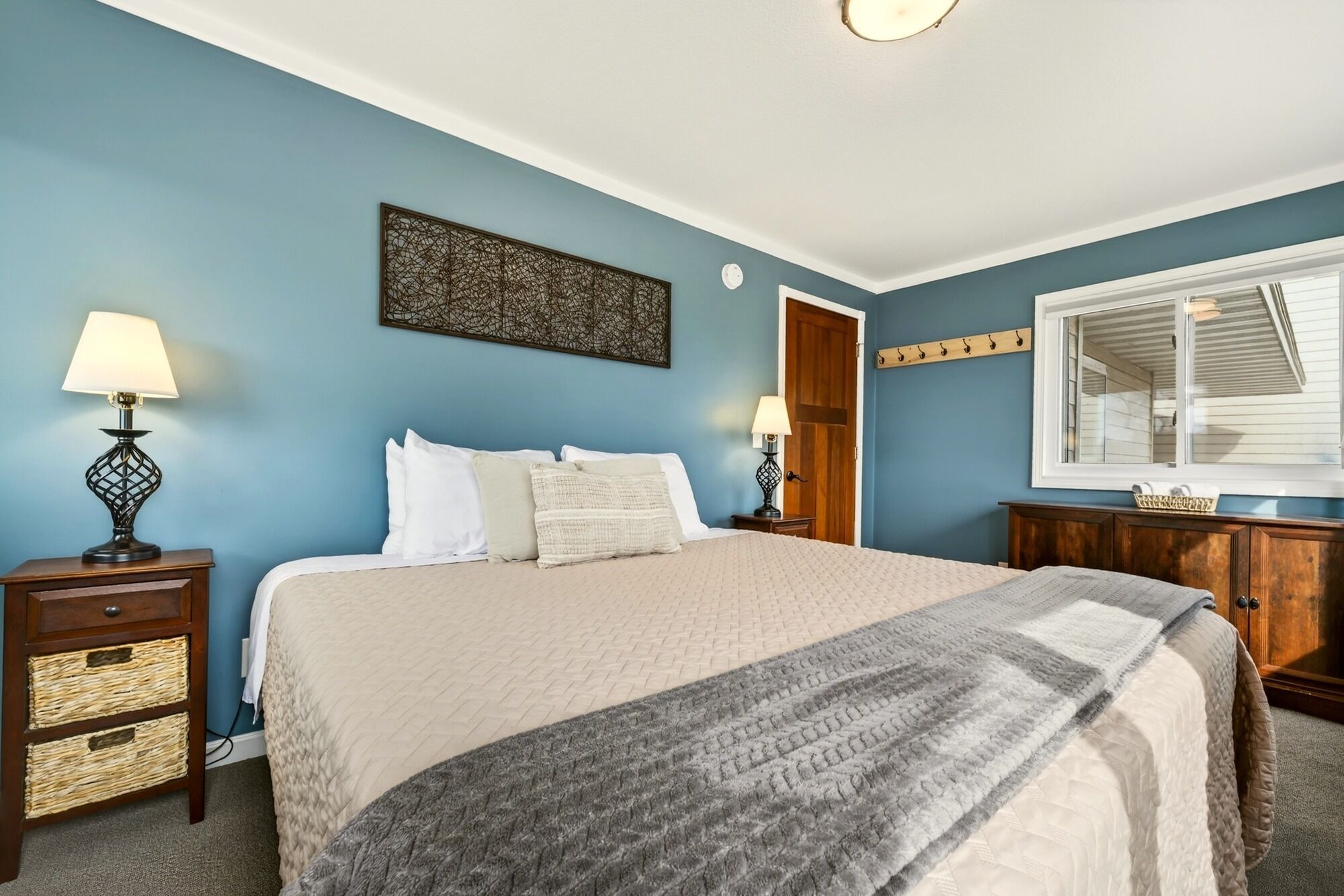 A bedroom with a bed, two bedside tables, a dresser, a window, and a wall art piece.