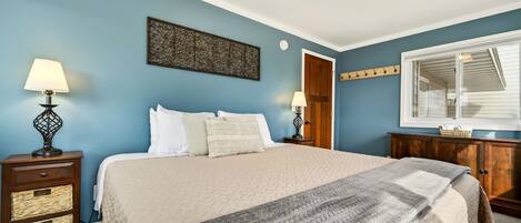 A bedroom with a bed, two bedside tables, a dresser, a window, and a wall art piece.