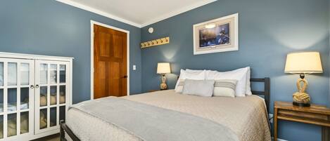 Un dormitorio con cama, mesitas de noche, un armario, una puerta y un cuadro colgado en la pared.