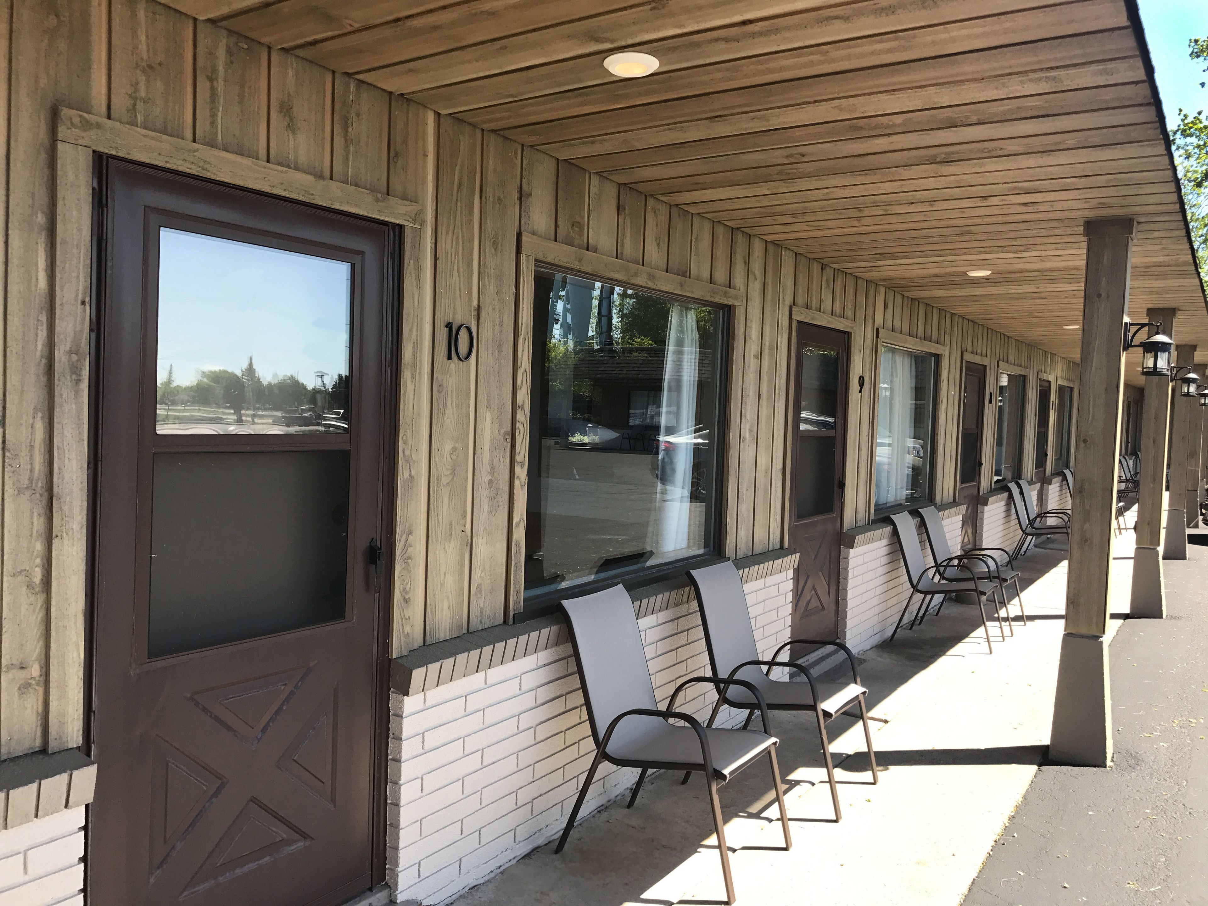 A covered outdoor seating area with wooden walls and a brick base, featuring numbered doors and metal chairs.