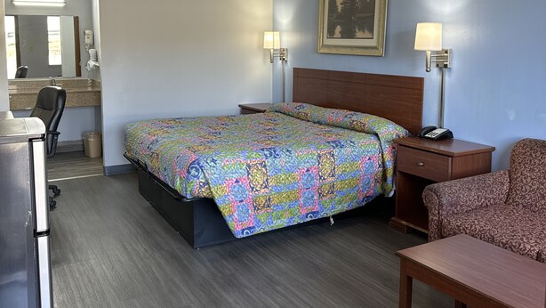 A hotel room with a bed, desk, chair, and a painting on the wall. - Executive Inn (West Columbia)