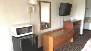 A hotel room with a bed, a wooden dresser, a black refrigerator, a white microwave, a television mounted on the wall, and a trash can. - Executive Inn (West Columbia)