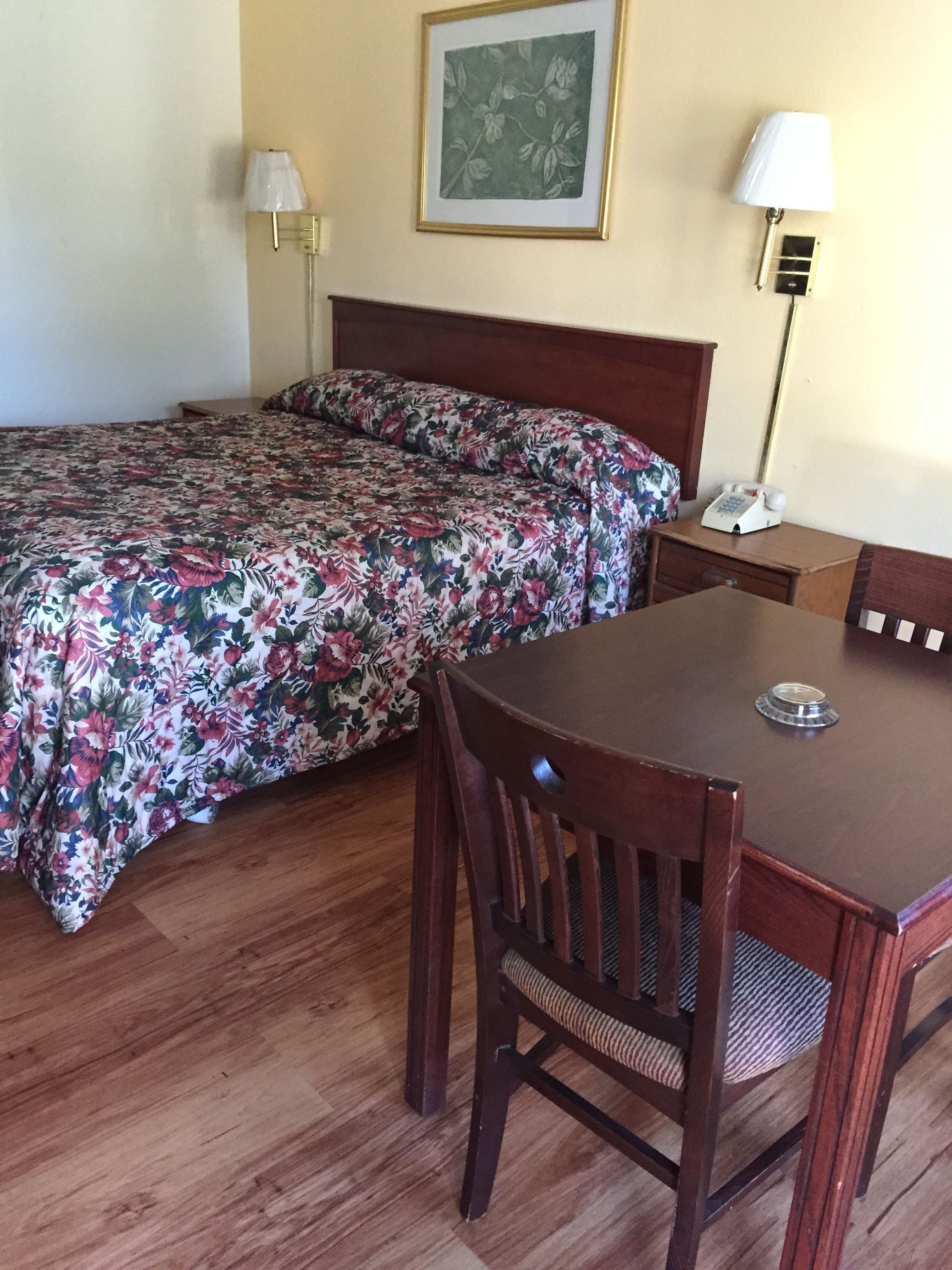 Ein Hotelzimmer mit Bett, Nachttisch aus Holz, Schreibtisch mit Telefon und einem Sessel.