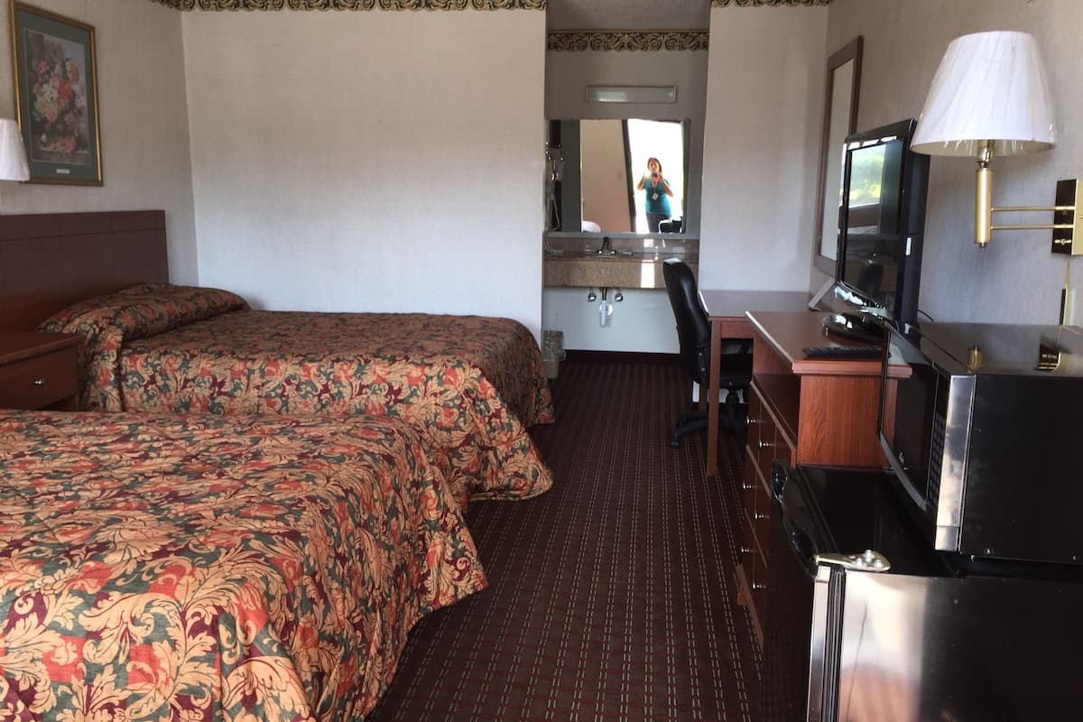 Quarto de hotel com duas camas, uma escrivaninha com computador, televisão e abajur.