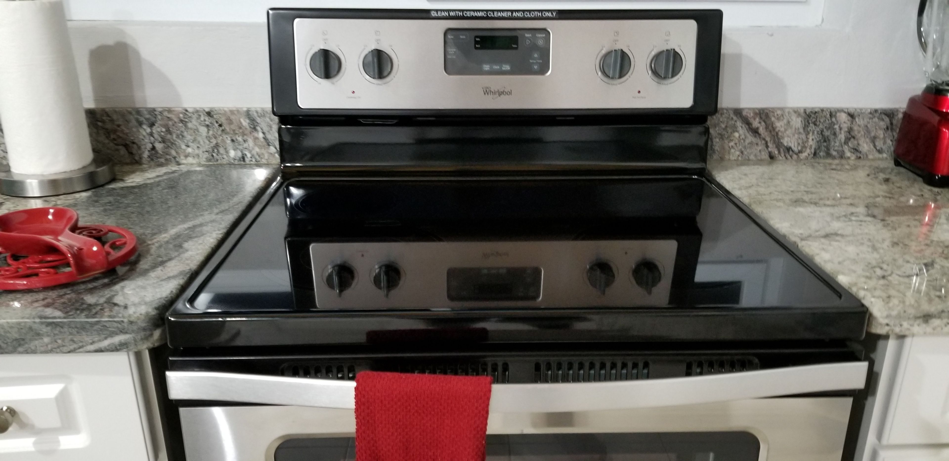A Whirlpool stove with a digital control panel, a red towel hanging on the oven door, and a granite countertop.