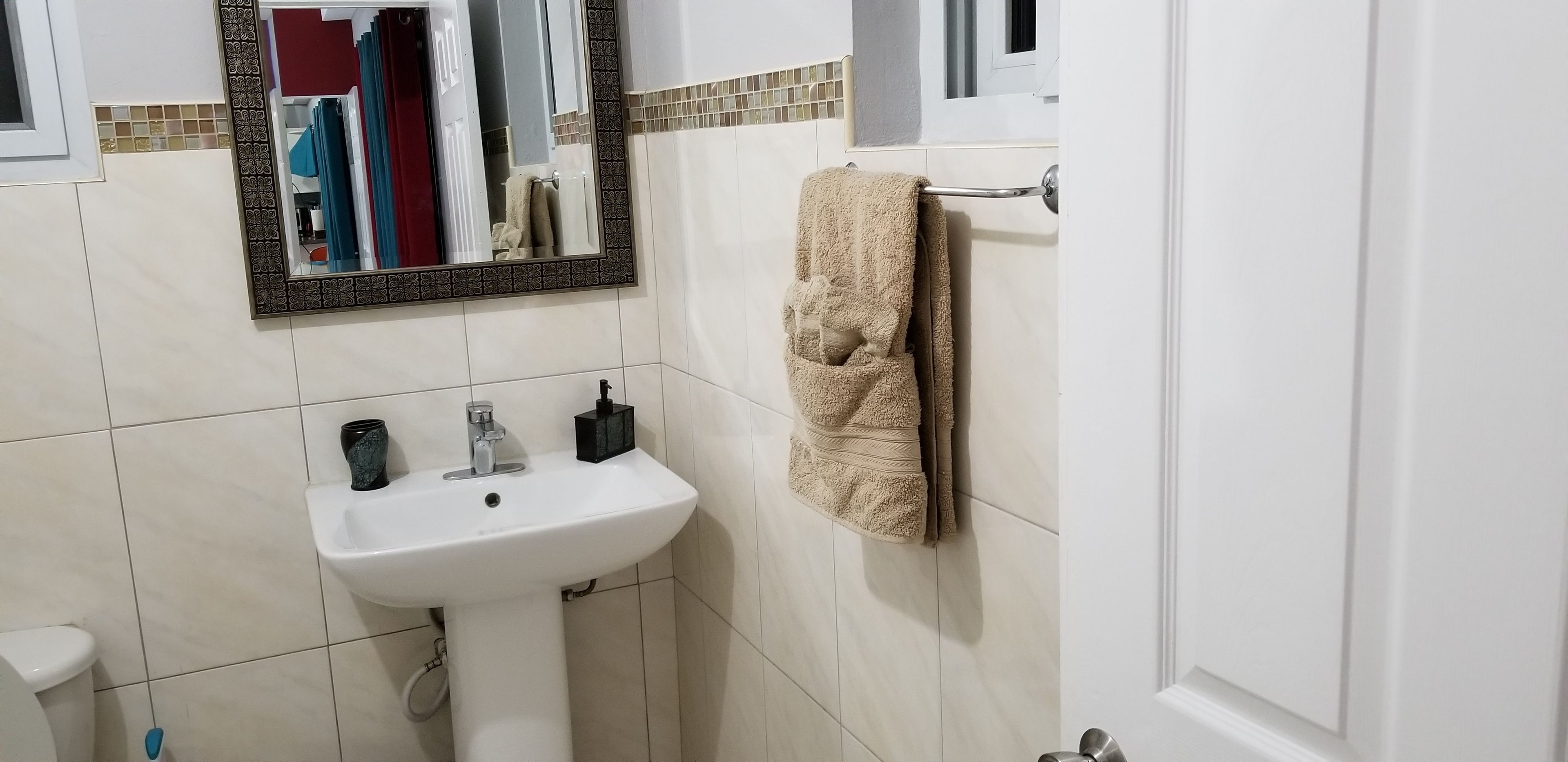 Une salle de bain avec un lavabo blanc, un miroir doté d’un cadre décoratif et une serviette suspendue à un porte-serviettes.
