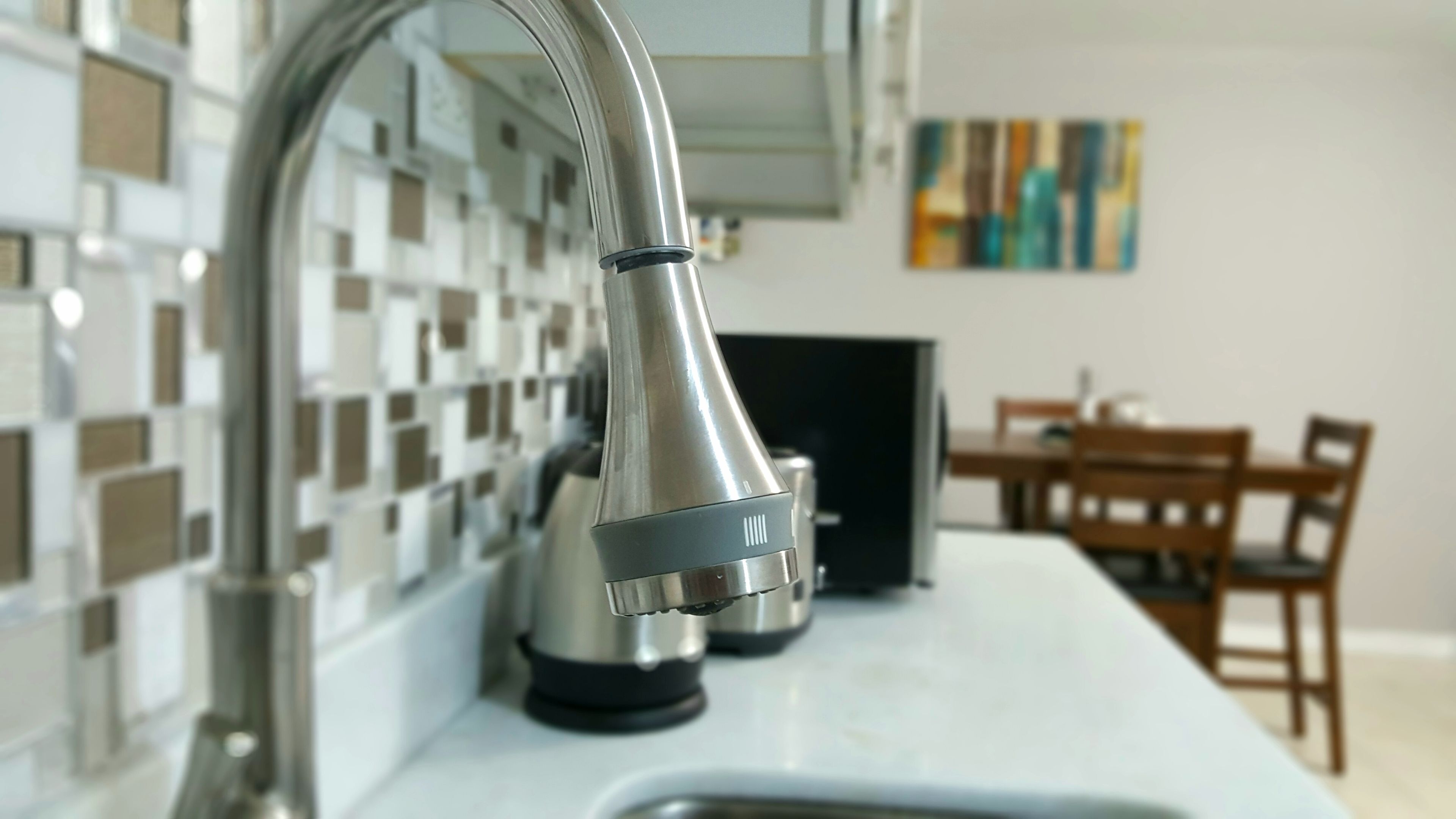 A kitchen with a modern faucet, a tiled backsplash, and a dining area with a table and chairs.