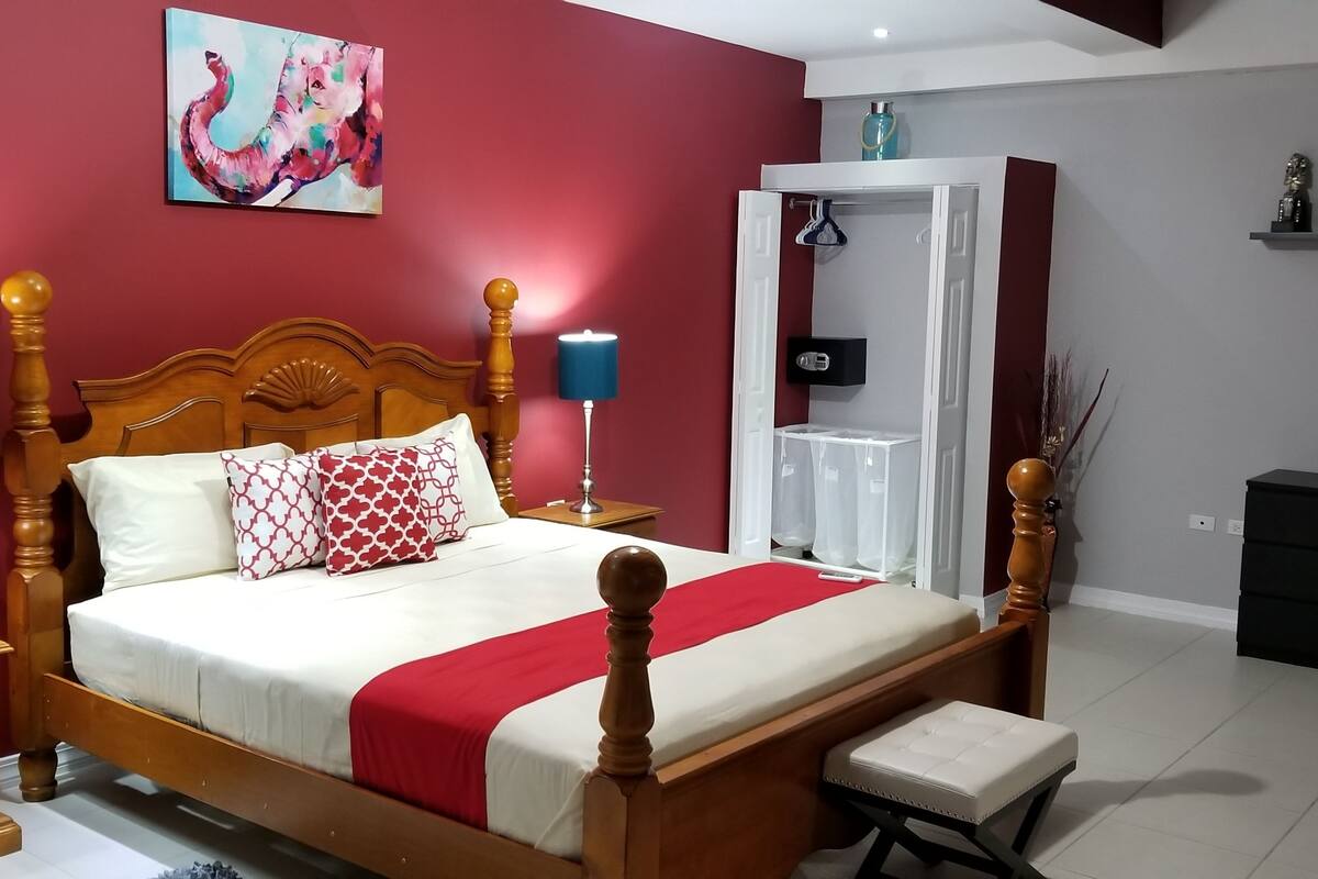 Une chambre à coucher avec un lit en bois, des murs rouges, une table de chevet avec une lampe et un banc.