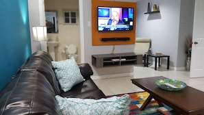 Una sala de estar con un sofá de cuero marrón, un televisor montado en la pared, una mesita con un cuenco y una alfombra colorida.