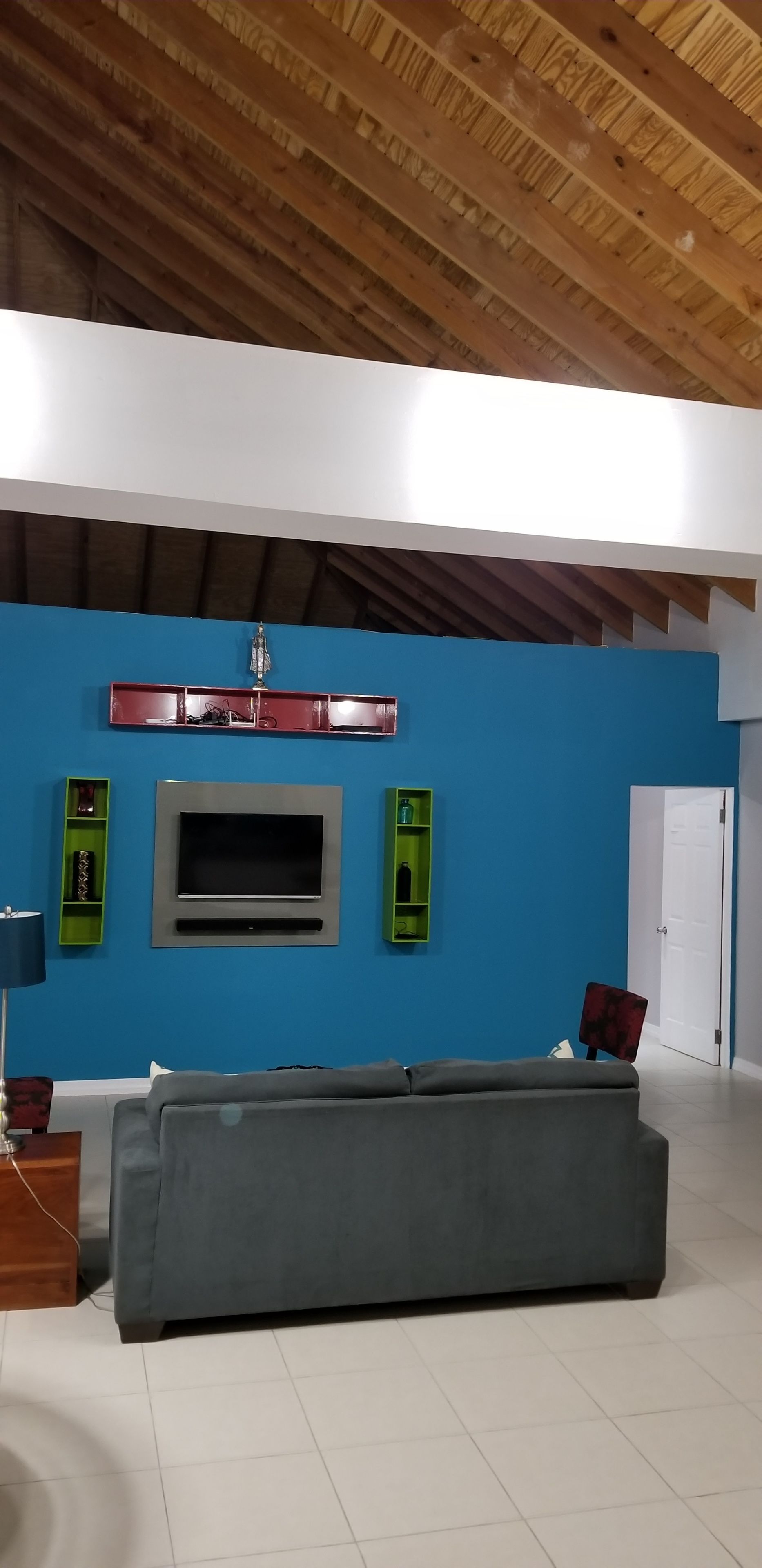 Un salon moderne avec un mur bleu, un canapé gris, un téléviseur à écran plat et des étagères vertes.