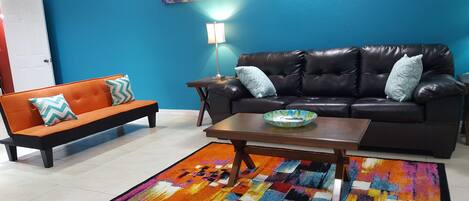 A living room with a black leather sofa, an orange sofa, a coffee table, and a colorful rug.