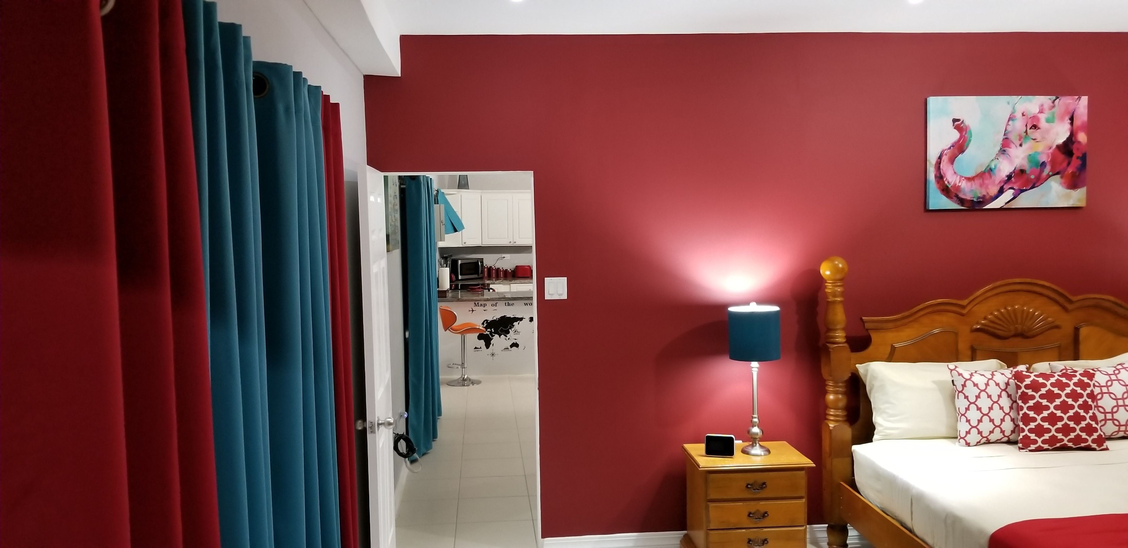 A bedroom with a wooden bed, a nightstand with a lamp, and a red wall with a painting.
