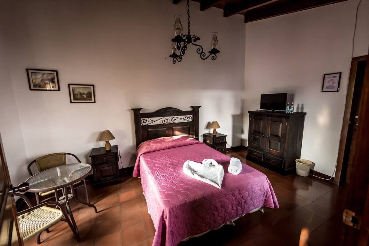 Un dormitorio con cama, una silla, una mesa, un aparador y un televisor.