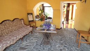 Una habitación con piso de piedra, un sof á, una mesa con un florero y un letrero en la pared.