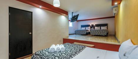 A hotel room with a bed, a sofa bed, a ceiling-mounted projector, and a door.