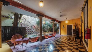 Piso xadrez, área de estar ao ar livre com mesas e cadeiras, e uma escada que leva a um andar superior.