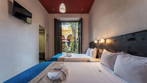 Quarto de hotel com duas camas, televisão na parede, luminária no teto e vista para o pátio.