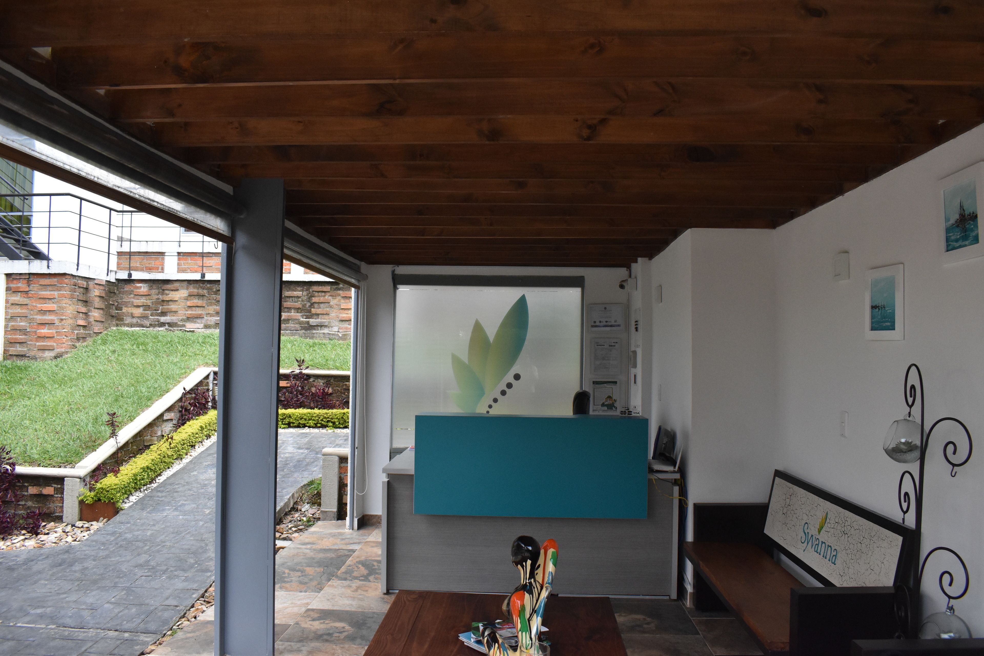 A reception area with a wooden ceiling, a reception desk, a bench, and a view of a brick building and greenery outside.