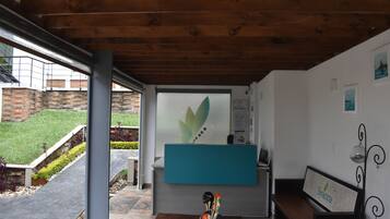 A reception area with a wooden ceiling, a reception desk, a bench, and a view of a brick building and greenery outside.