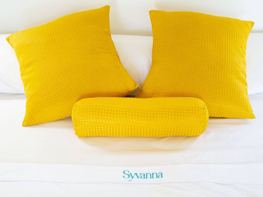 A bed with white bedding and three yellow pillows.