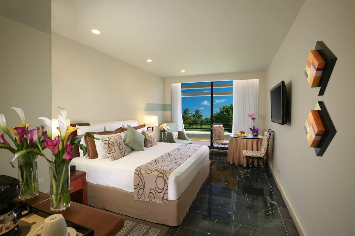 A hotel room with a large bed, a dining area, and a view of the outdoors.