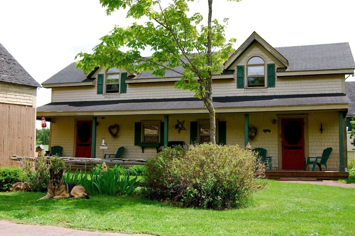 A two-story house with a porch, green shutters, and a red door.