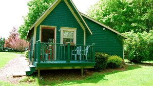 A small, green wooden house with a porch and a door open to the inside. - Bugaboo Cottages (Central Bedeque)