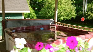 A hot tub with a wooden deck and a metal railing, surrounded by greenery and flowers. - Bugaboo Cottages (Central Bedeque)