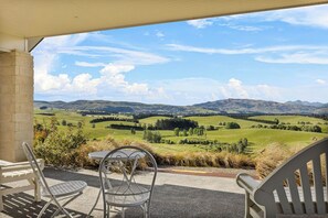 A patio with two metal chairs and a table, overlooking a scenic landscape with rolling hills and a clear sky.